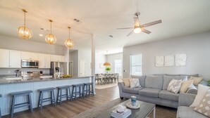 A modern kitchen with stainless steel appliances, a bar area, and a dining space with a table and chairs. - Tidepool by Avantstay 2min Walk to Miramar Beach! (Miramar Beach)