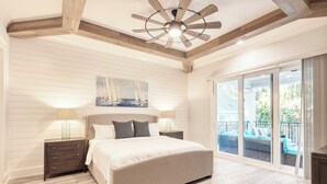 Une chambre dotée d’un grand lit, de poutres apparentes en bois au plafond, d’un ventilateur de plafond et offrant une vue sur le balcon extérieur.