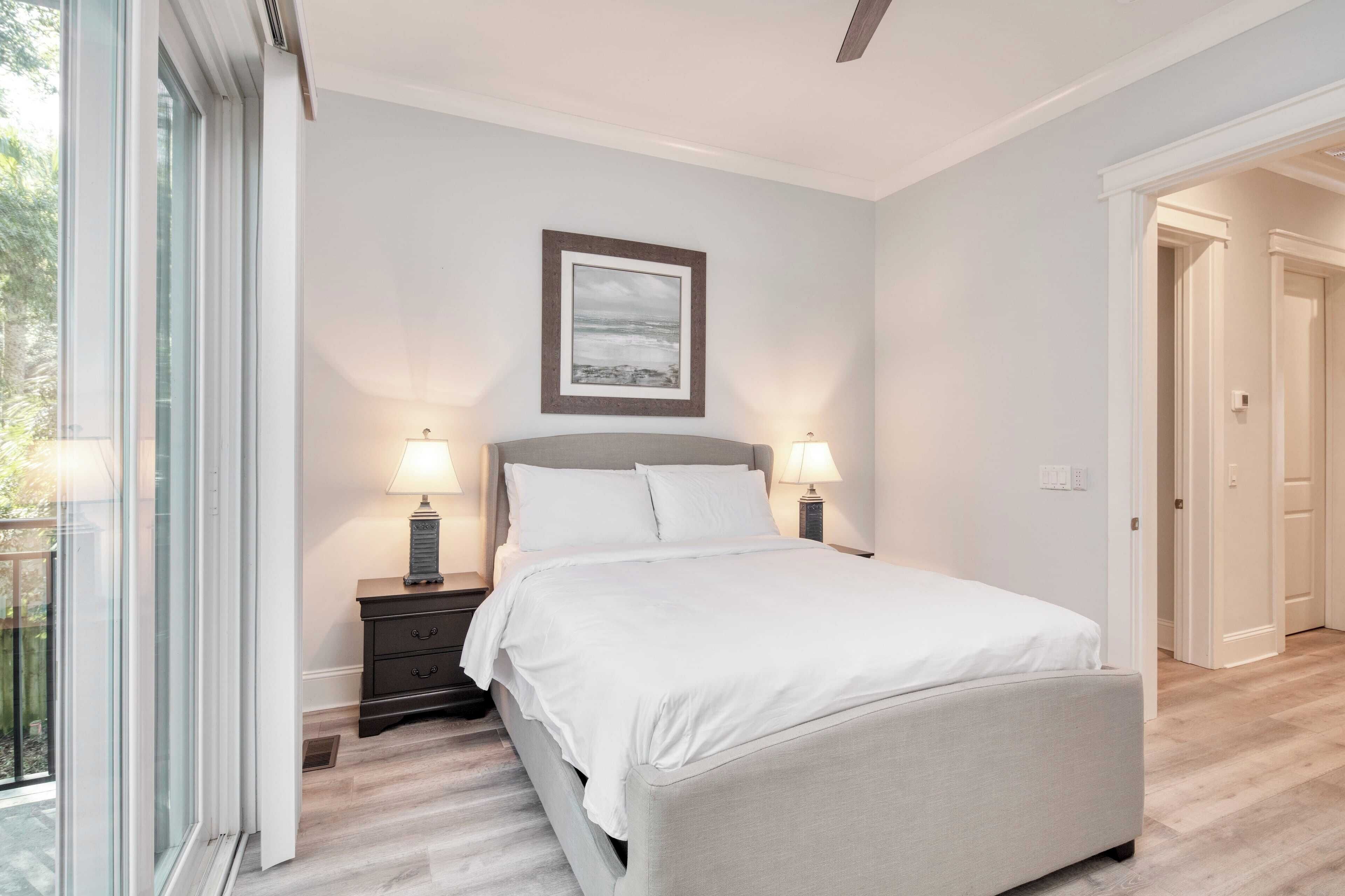 Une chambre à coucher avec un lit, des tables de chevet, un tableau encadré au mur et une porte donnant sur une autre pièce.