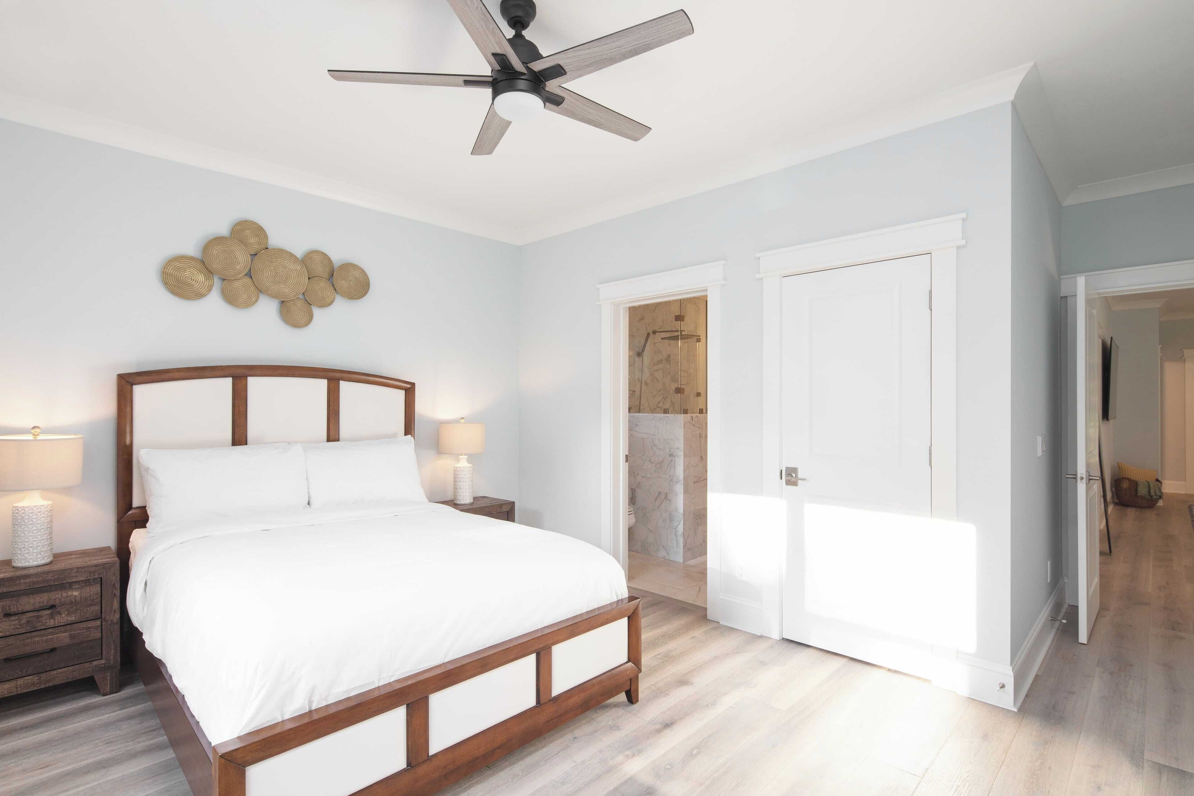 Une chambre à coucher avec un lit en bois, du linge de lit blanc, un ventilateur de plafond et un luminaire fixé au mur.