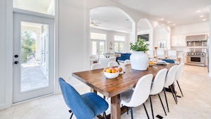 A spacious dining area with a wooden table, white and blue chairs, and a large vase of flowers. - Miramar Manor by Avantstay Walk to the Beach! (Miramar Beach)