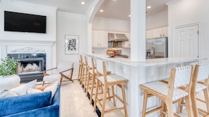 A modern kitchen with white cabinetry, a stainless steel refrigerator, and a bar area with wooden chairs. - Miramar Manor by Avantstay Walk to the Beach! (Miramar Beach)