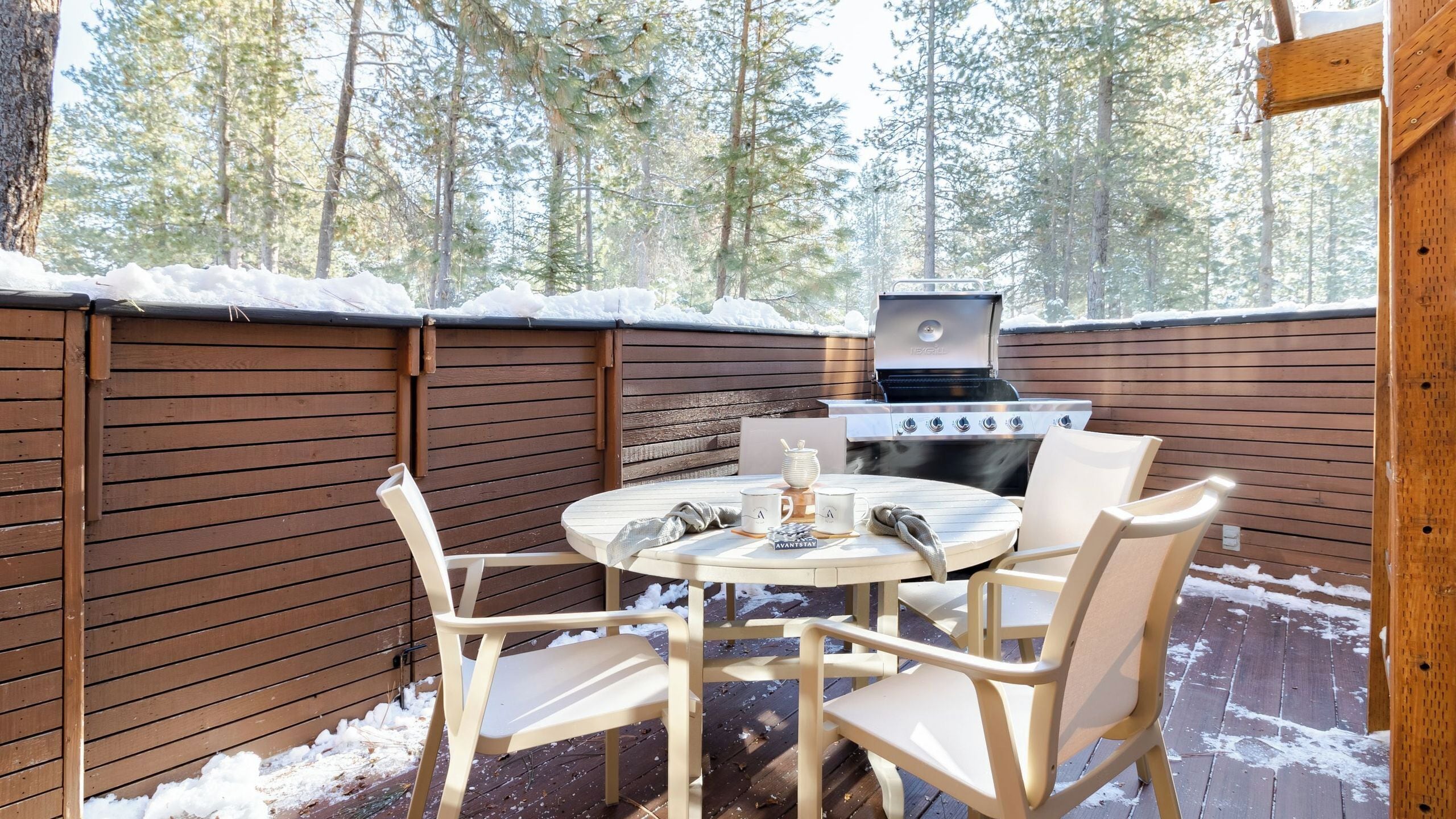 A wooden deck with a grill, a round table, and four chairs.
