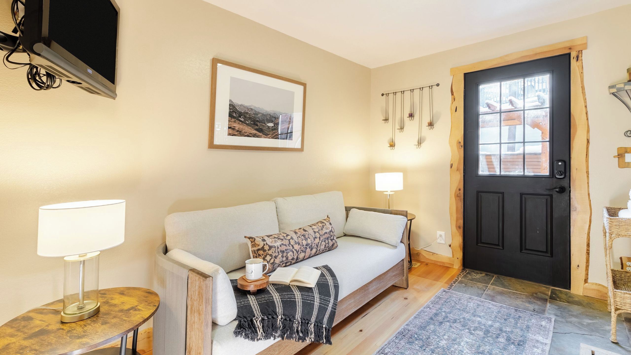 A cozy living room with a sofa, a lamp, a framed picture, a door, and a window.