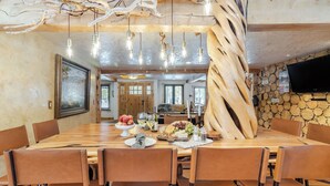A dining area with a long wooden table, leather chairs, and a rustic decor featuring wood and branches. - Base Camp by Avantstay Magical Cabin w/ Sauna, Hot Tub & Close to Snow & Golf (Bend)