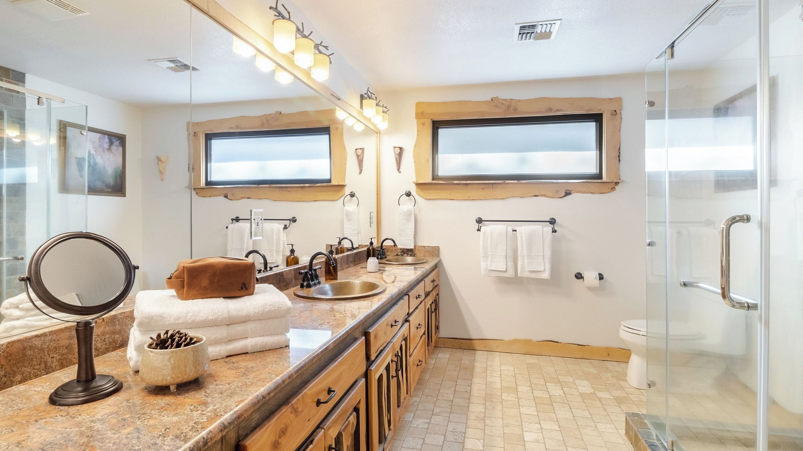 A bathroom with a vanity, two sinks, a mirror, a towel rack, and a shower area.
