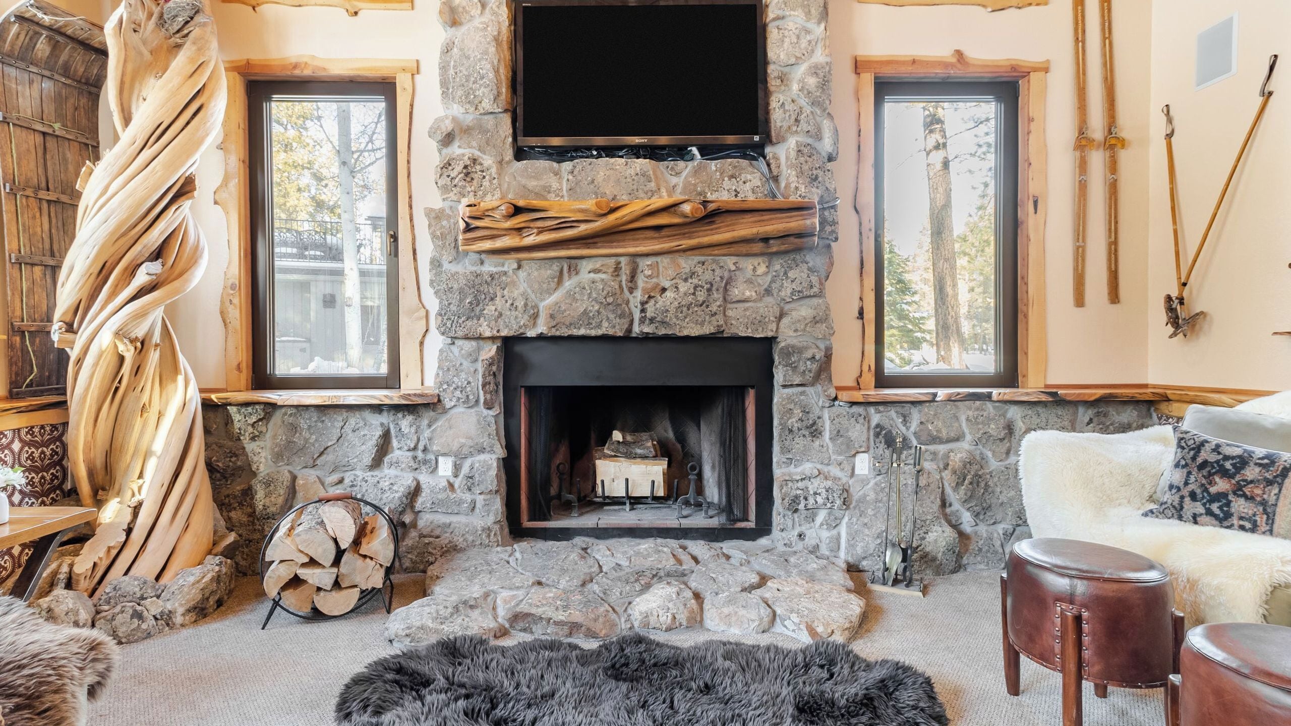 A stone fireplace with a TV above it, wooden logs, and skis on the wall.