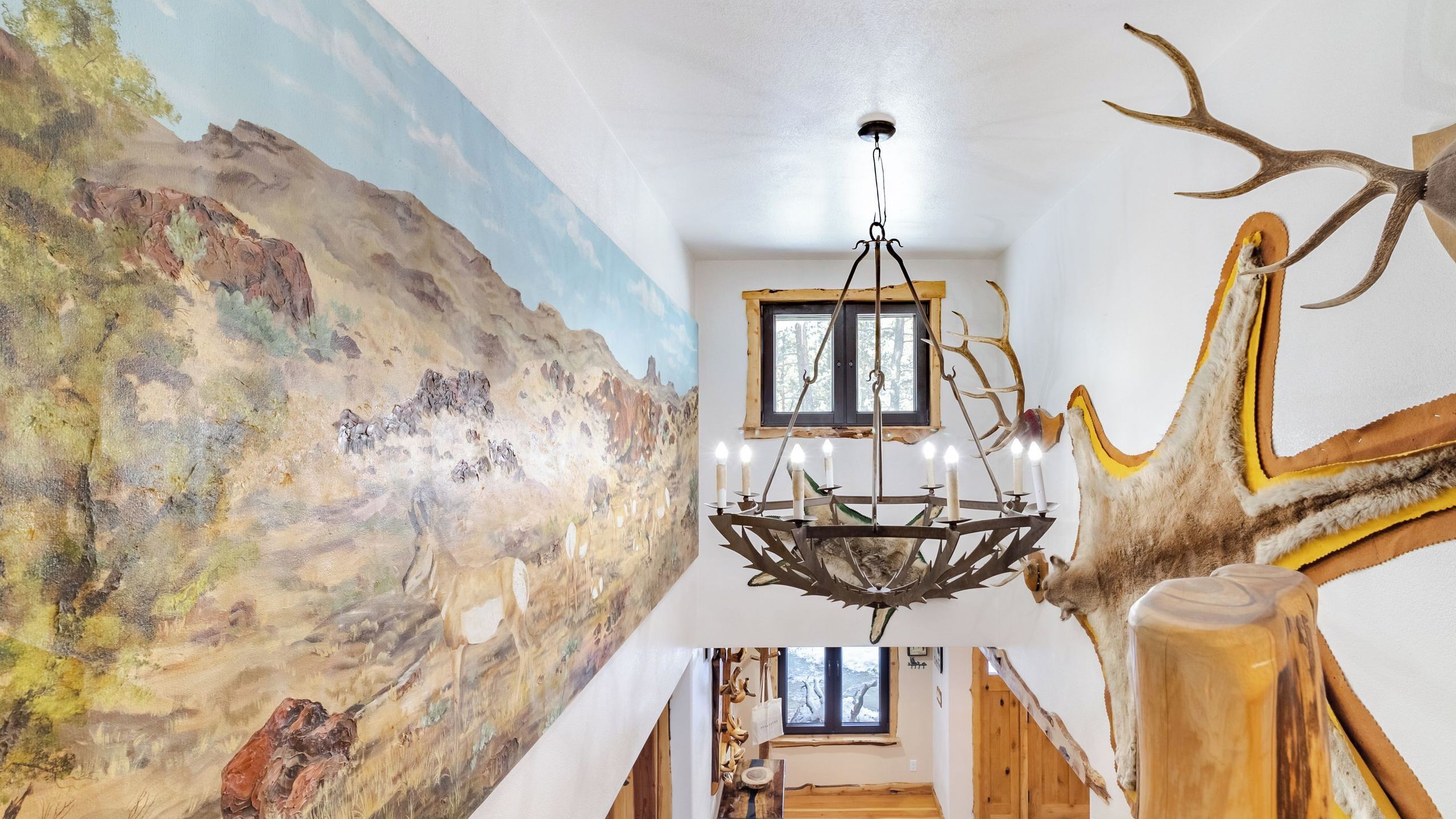 Une pièce ornée d’une fresque représentant un paysage désertique, d’un lustre et d’une tête de cerf fixée au mur.