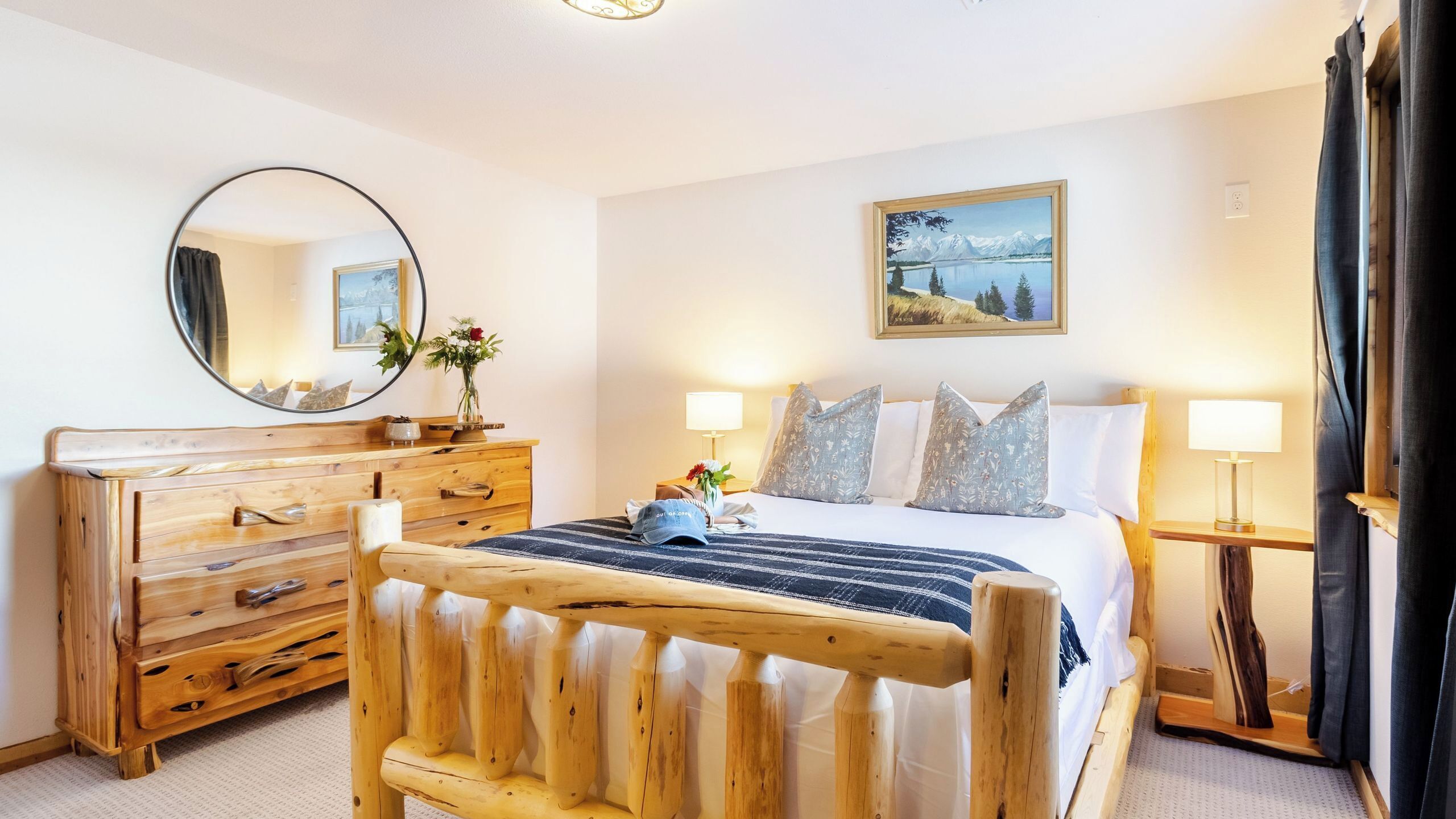 Habitación de hotel con cama de madera, cómoda, espejo, un cuadro y dos lámparas de noche.