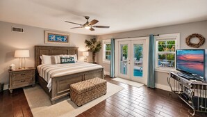 A bedroom with a bed, nightstands, a television, and a view of a pool through a sliding glass door. - Oasis with Heated Pool (Siesta key)