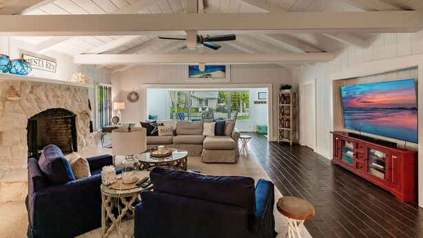 A spacious living room with a stone fireplace, a large flat-screen TV, and a ceiling fan. - Oasis with Heated Pool (Siesta key)