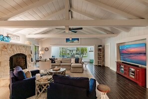A spacious living room with a stone fireplace, a large flat-screen TV, and a ceiling fan.