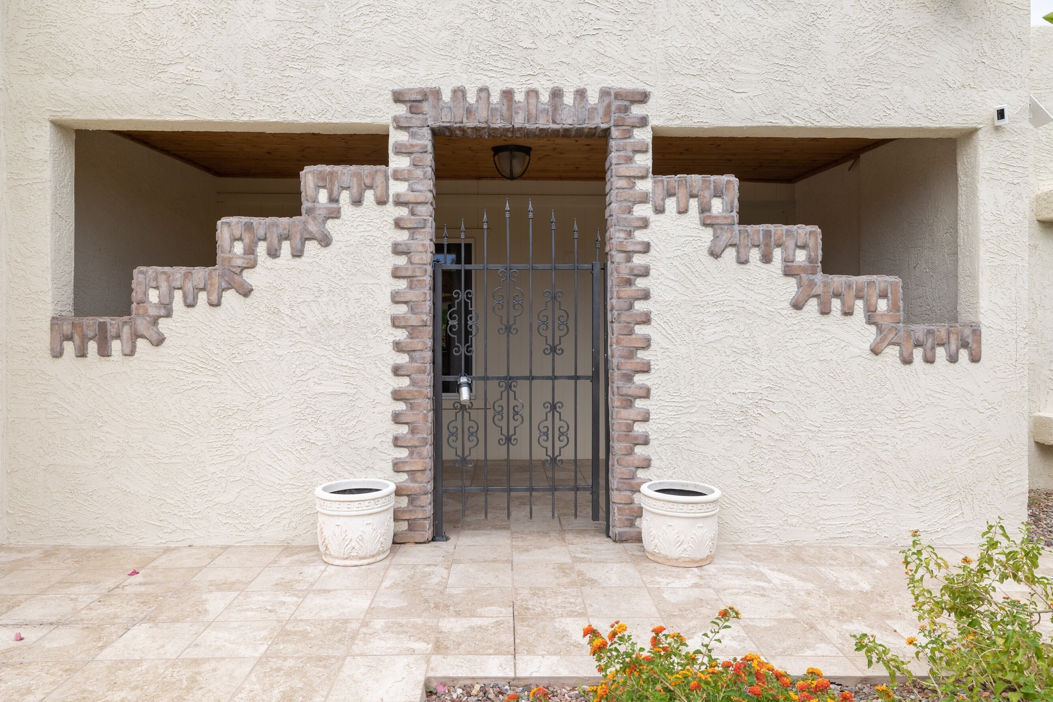 A building entrance with a brick staircase leading up to a metal gate. There are two white planters on either side of the gate.