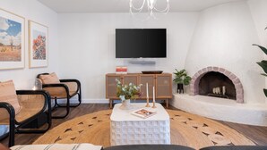 A living room with a flat-screen TV, a fireplace, wicker chairs, a coffee table, and a chandelier.