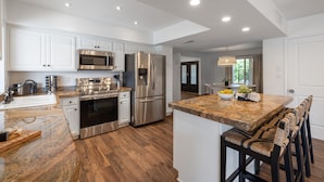 A modern kitchen with white cabinets, stainless steel appliances, a granite countertop, and a bar seating area.