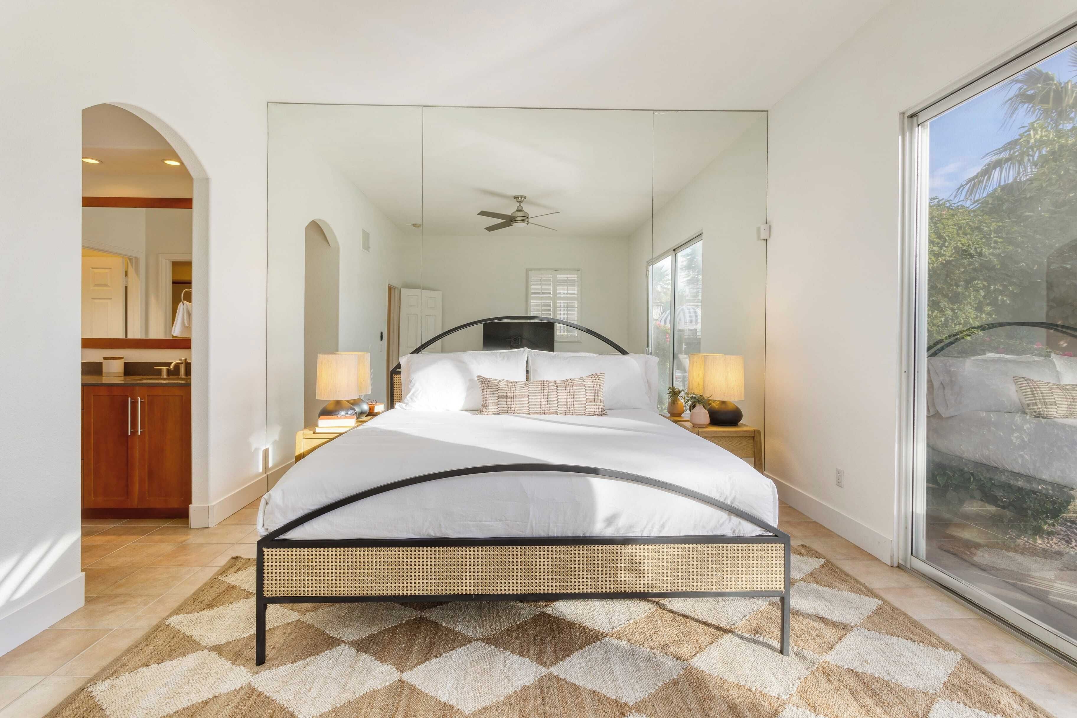 Une chambre à coucher avec un lit, un ventilateur de plafond, une grande fenêtre et une vue sur l’extérieur.