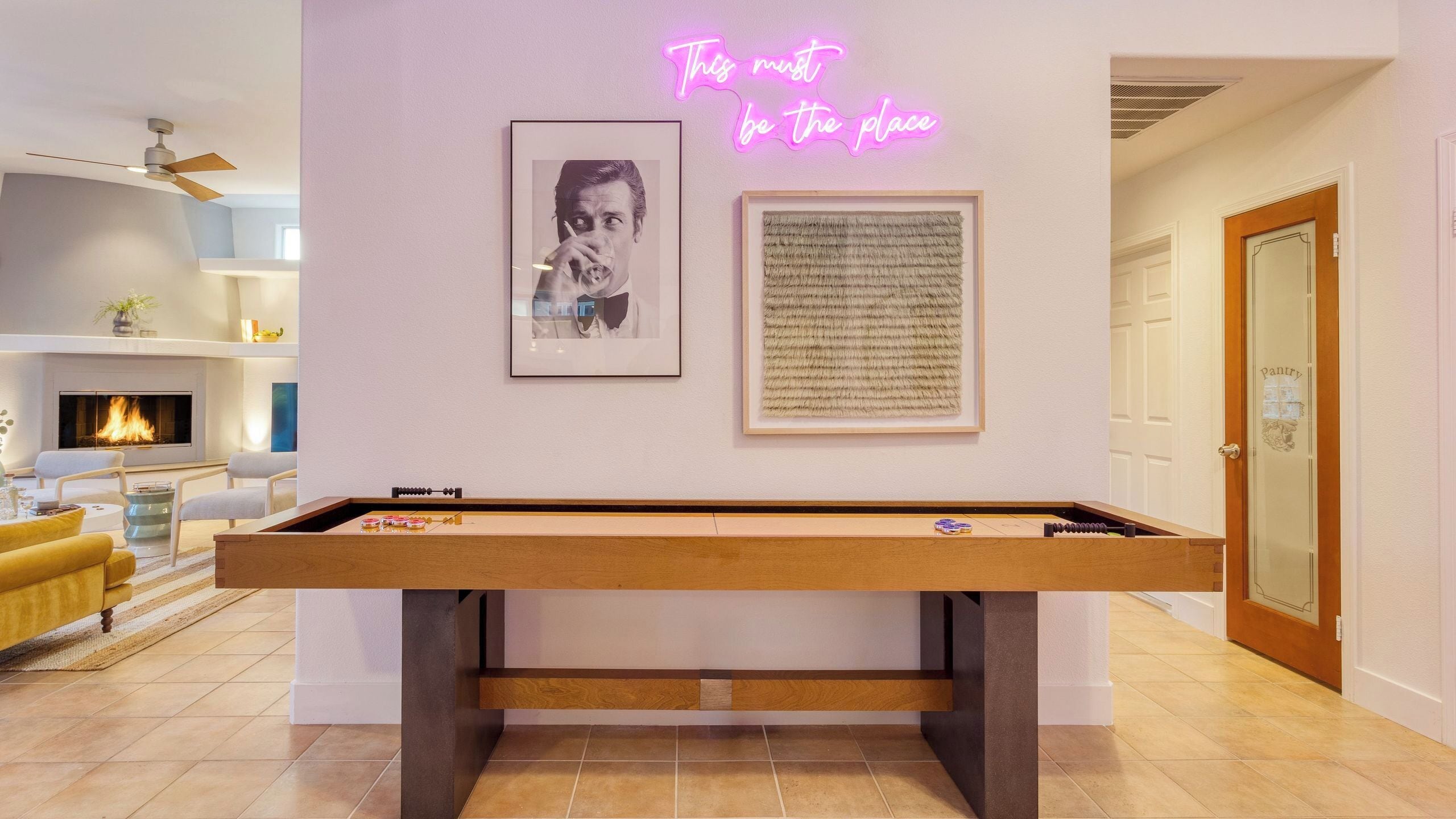 A pool table with a neon sign, framed artwork, and a fireplace in a modern living room.