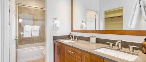 Un baño con cabina de ducha de vidrio, dos lavamanos, un espejo grande y muebles de madera.