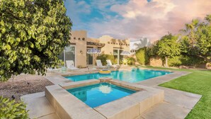 Piscina com espreguiçadeiras, um flutuador inflável pequeno e um edifício com estilo arquitetônico singular ao fundo.