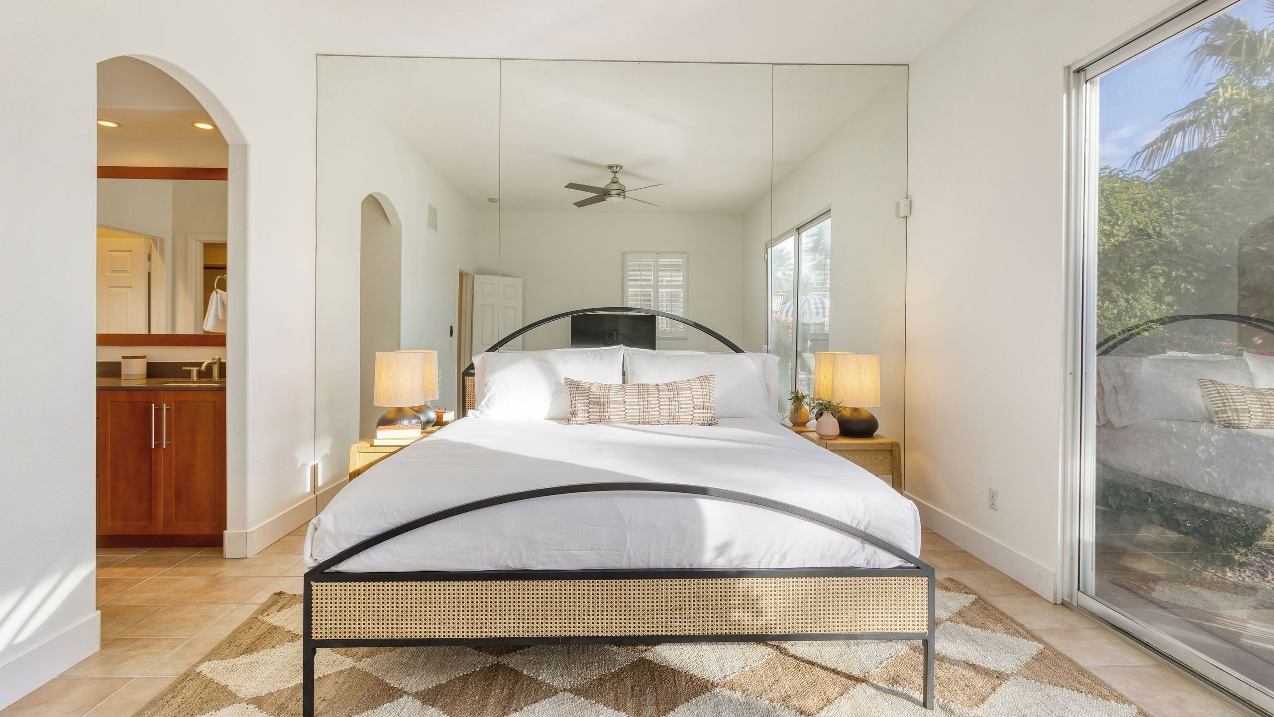 A bedroom with a bed, bedside lamps, a ceiling fan, and a large window.