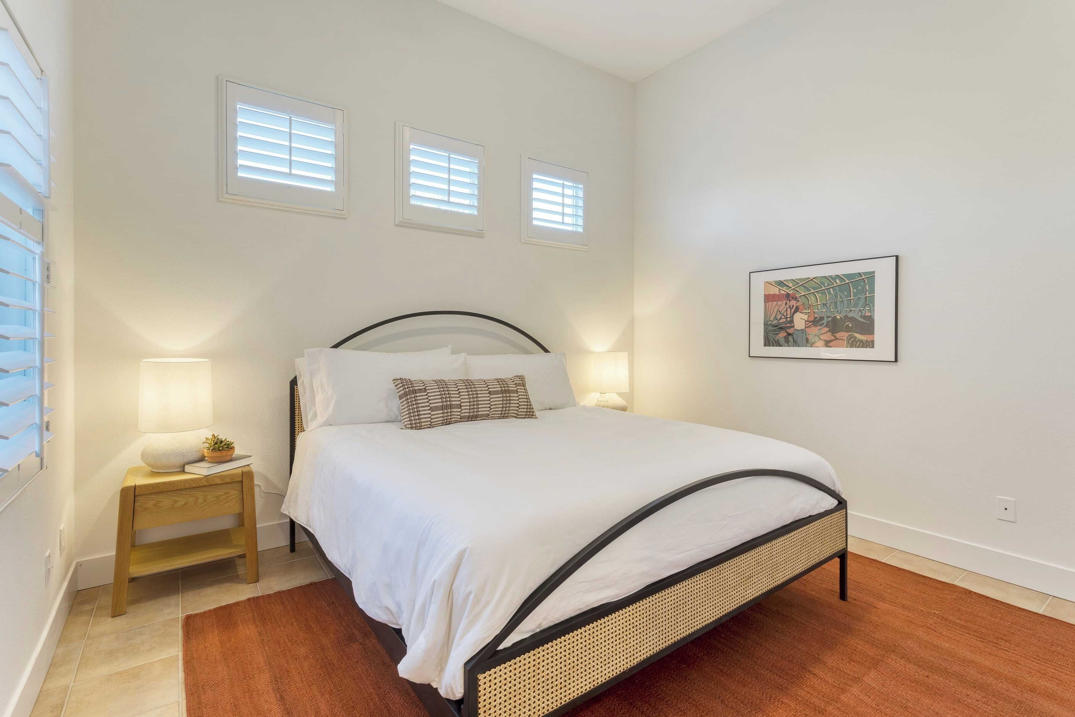 Een slaapkamer met een bed, nachtkastjes en een raam met jaloezieën.