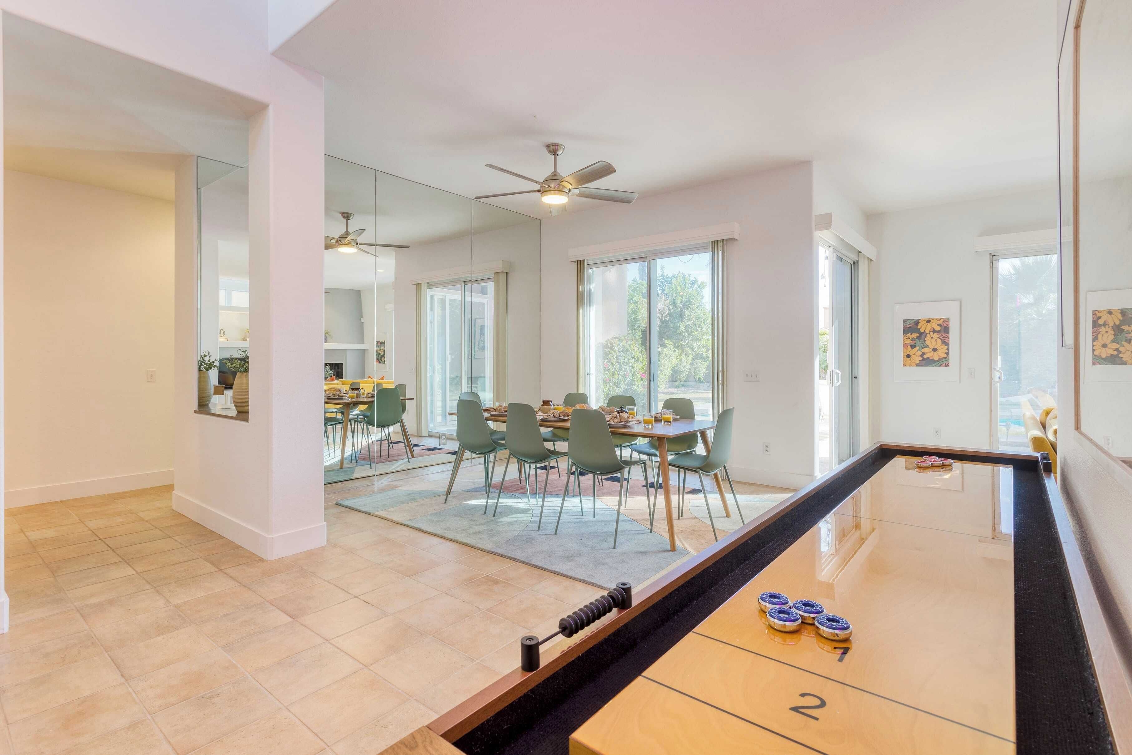 A spacious room with a pool table, a dining area with green chairs, and a ceiling fan.