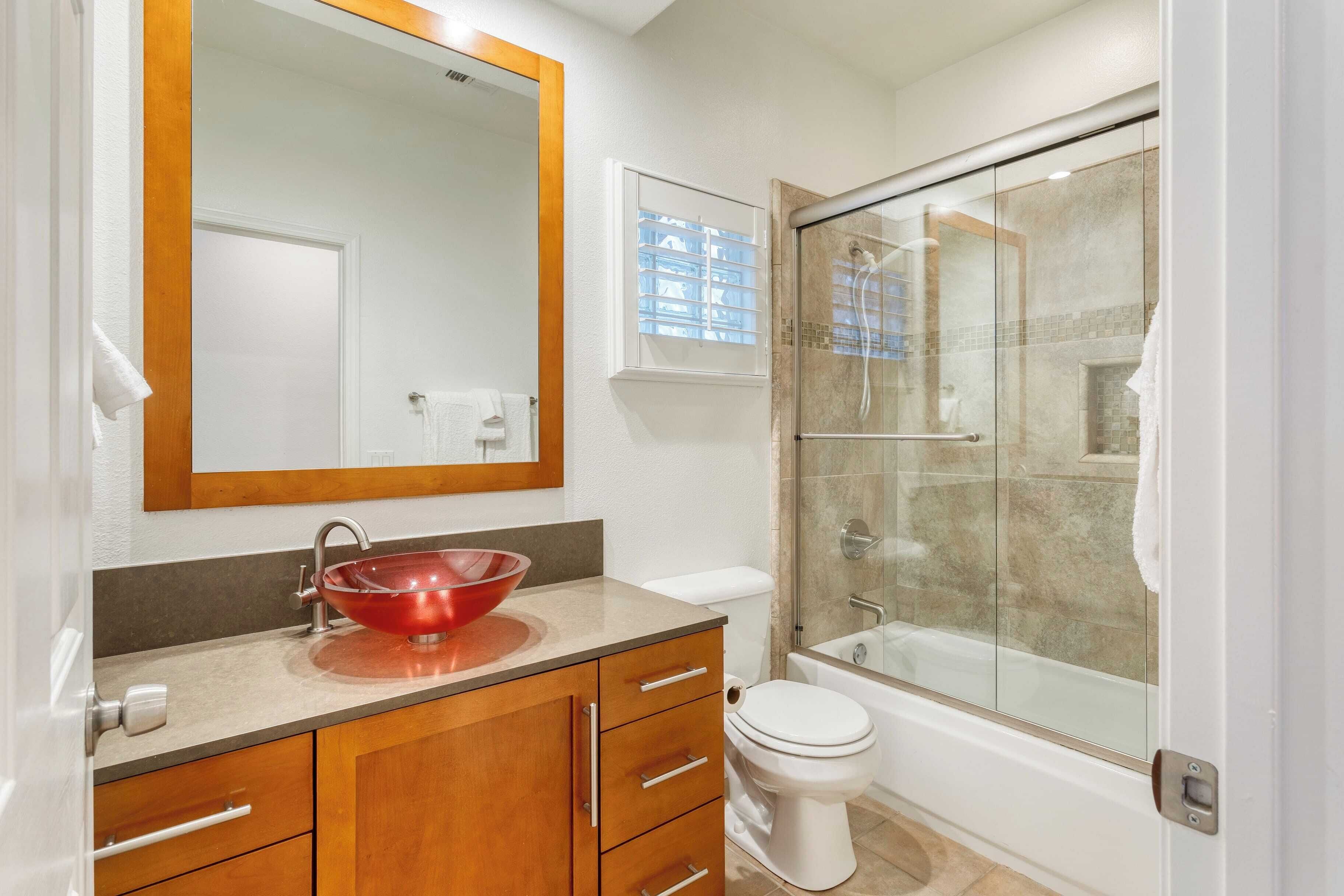 Une salle de bain avec un meuble-lavabo en bois, un lavabo rouge, des toilettes blanches et une douche à parois de verre.