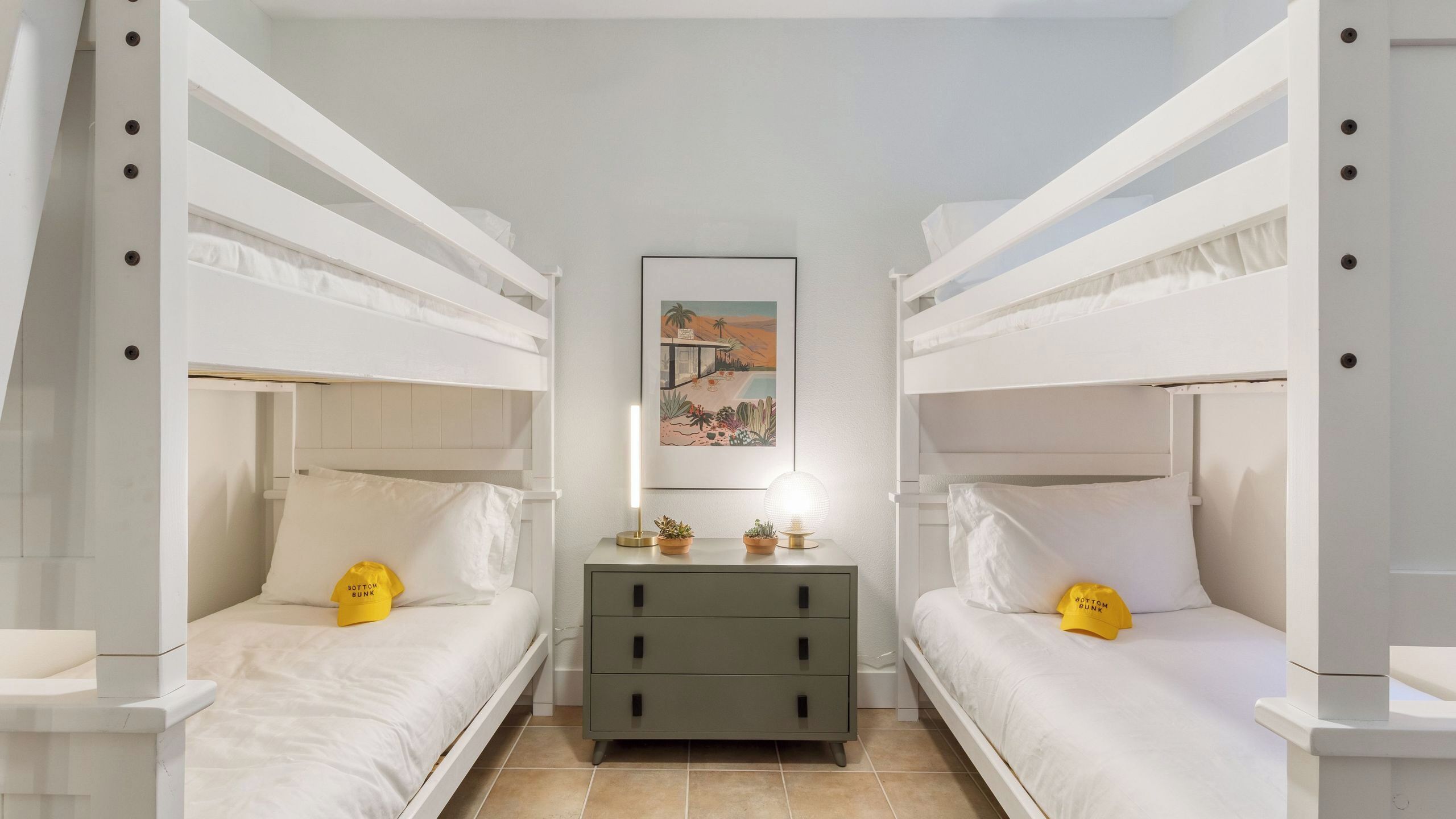Une chambre avec des lits superposés, une table de chevet, une commode et un tableau encadré au mur.