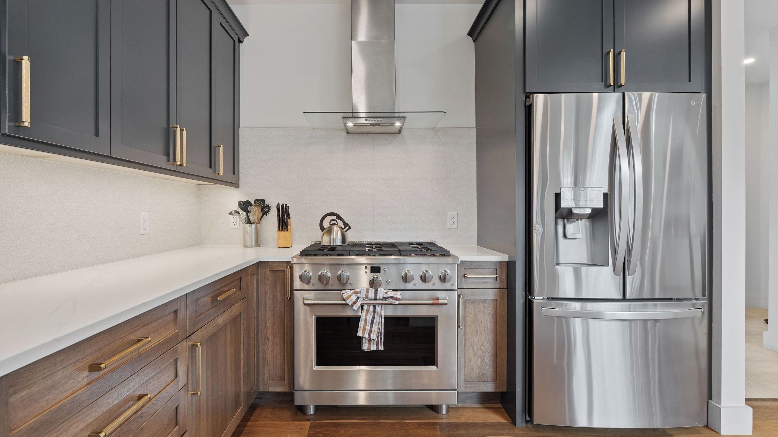 Une cuisine moderne avec des meubles de couleur sombre, des appareils électroménagers en acier inoxydable et un plan de travail en bois.