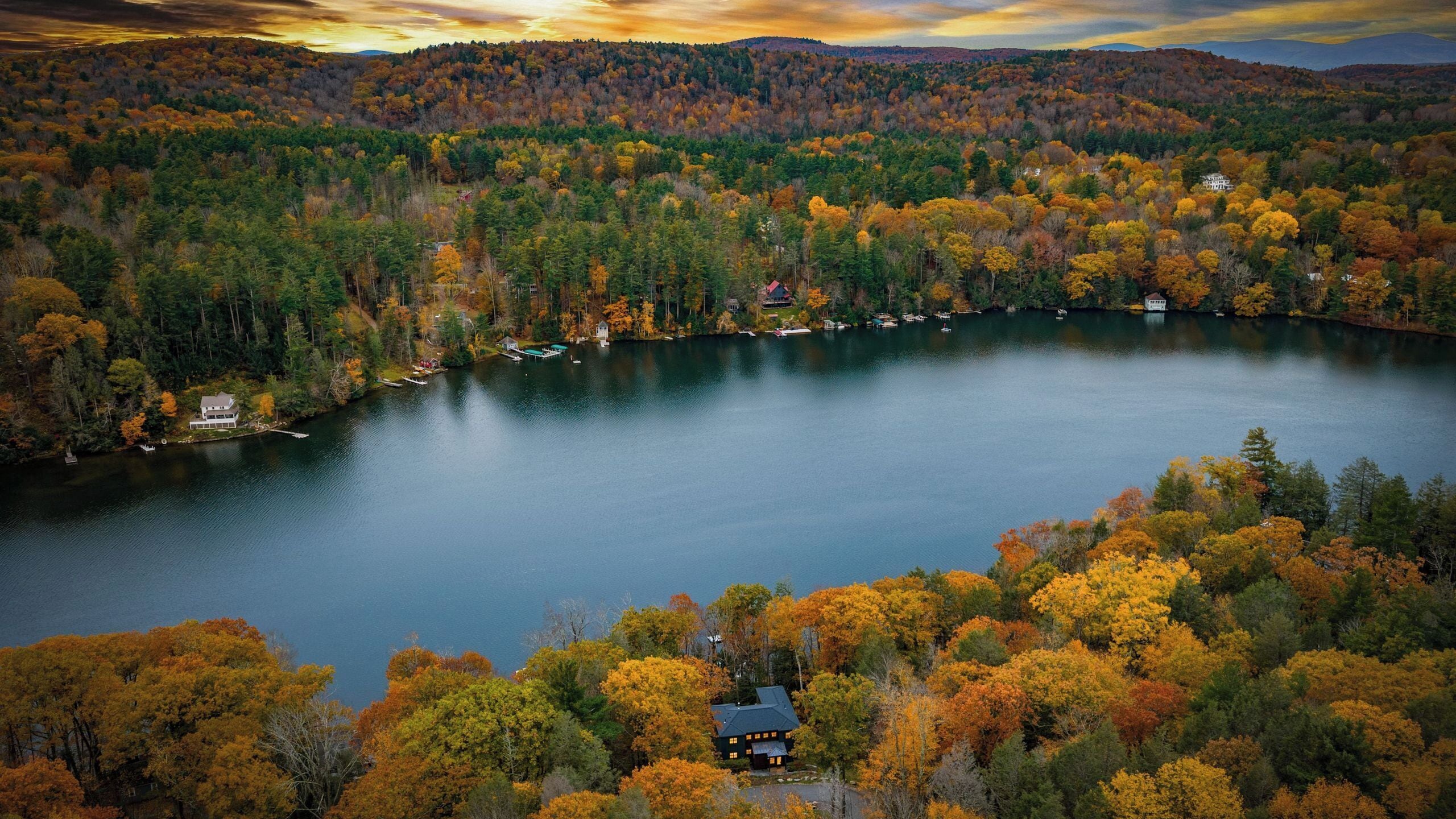 Un lac entouré d’arbres aux couleurs automnales et de maisons.