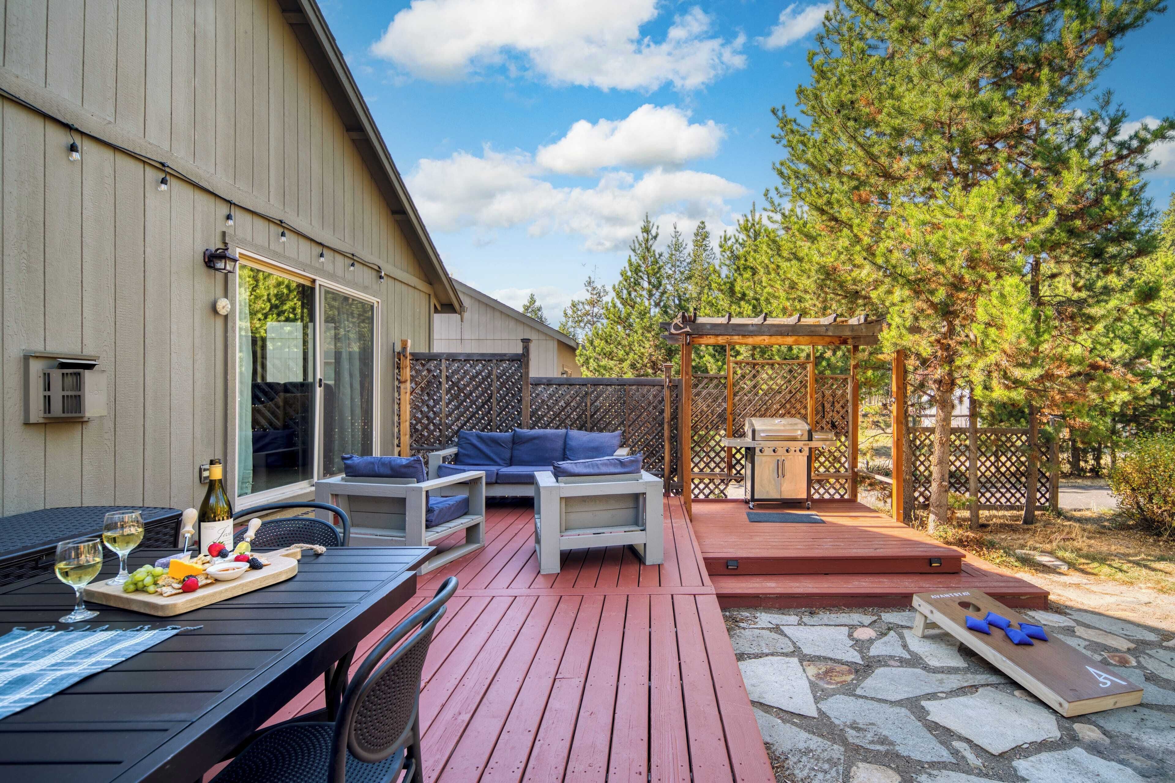 An outdoor patio with a wooden deck, a seating area with blue cushions, a pergola, and a stone fire pit.