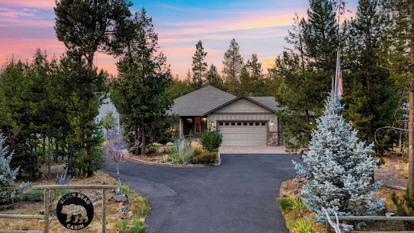 Une cabane avec un garage, entourée d’arbres et donnant sur une allée.