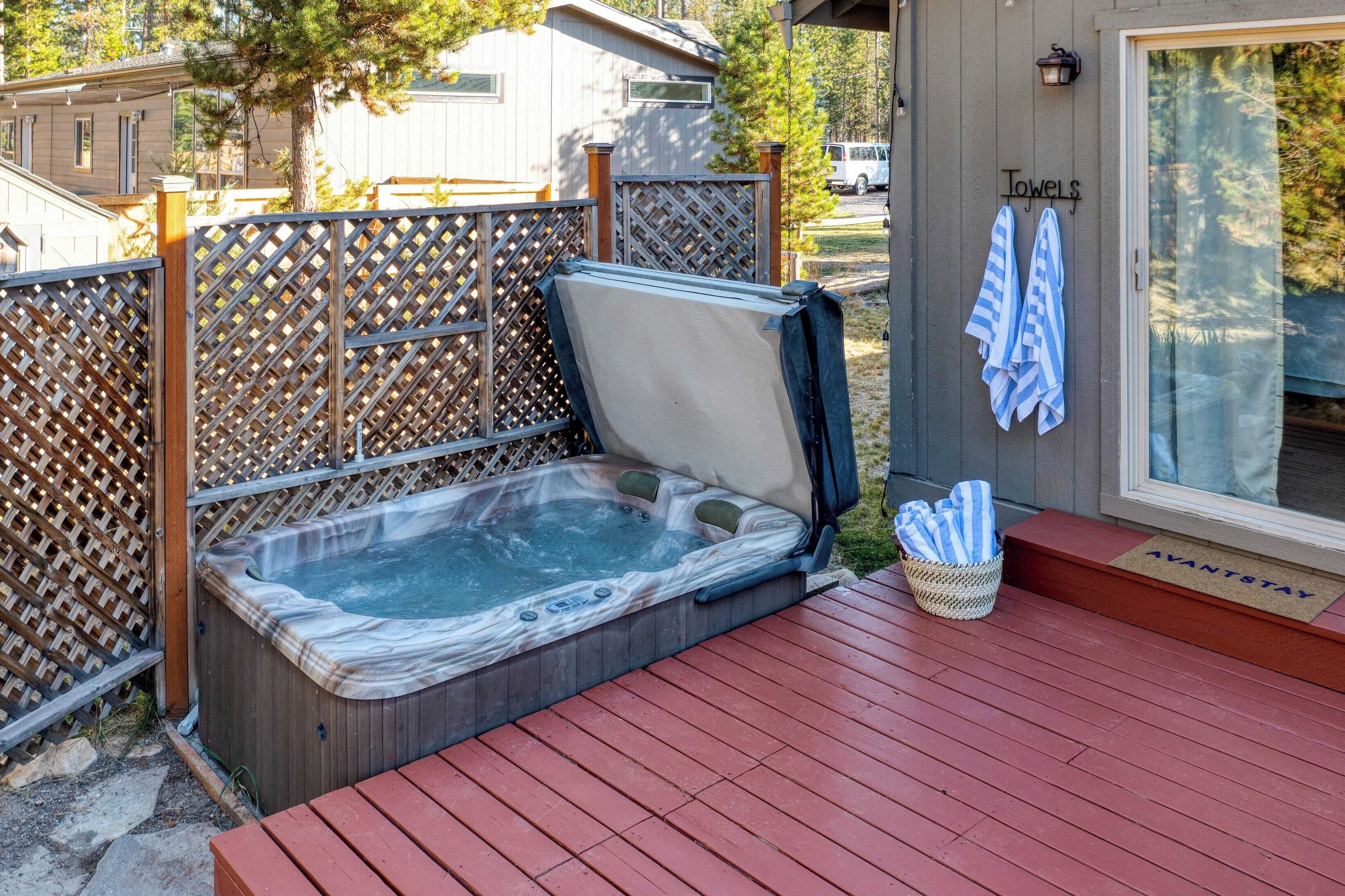 A hot tub on a wooden deck with a lattice fence, towels hanging on the wall, and a doormat with the text "AVANTSTAY".