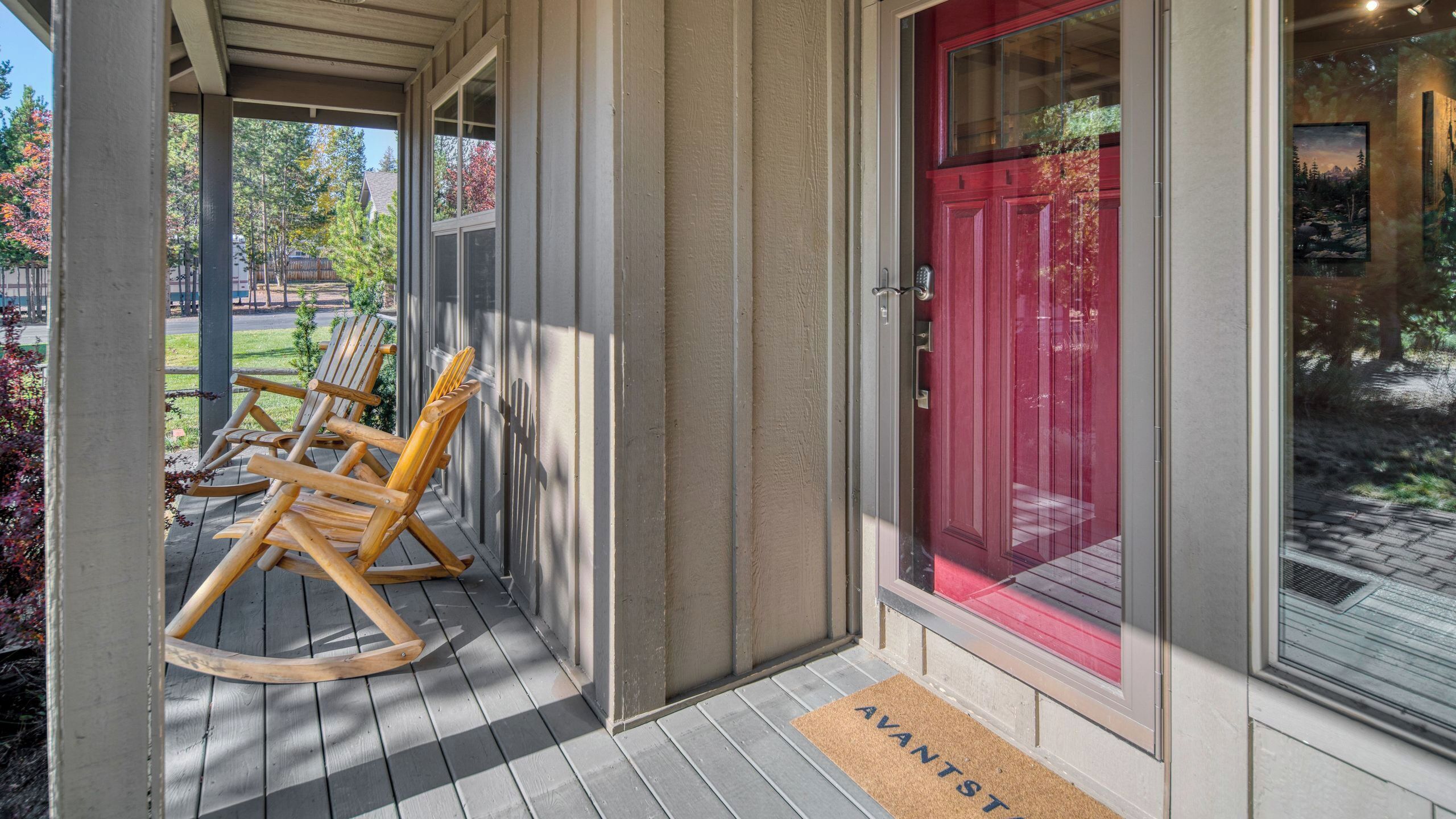 Une véranda en bois avec des fauteuils à bascule, une porte rouge et un paillasson sur lequel est écrit « VANTST ».