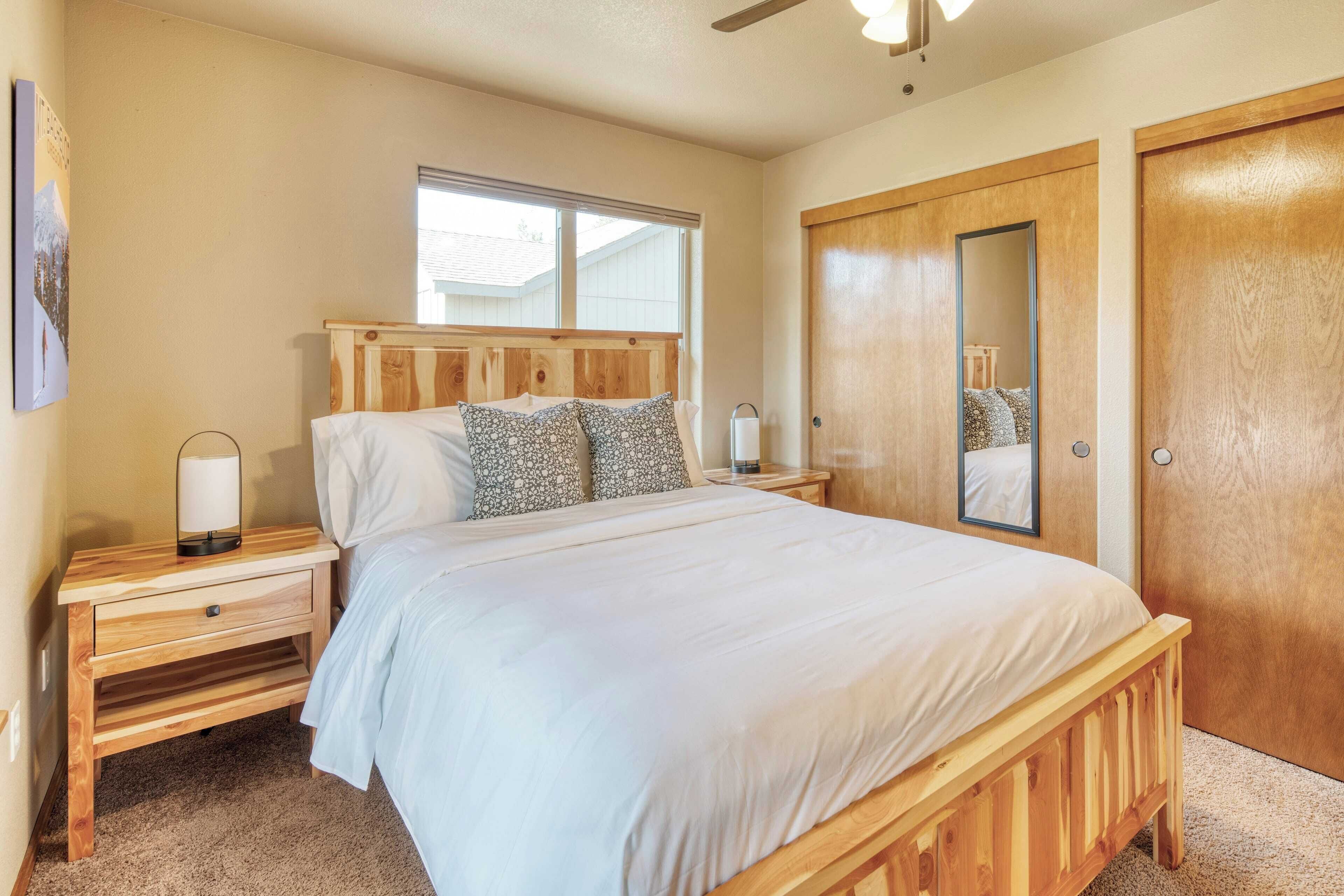 A bedroom with a wooden bed, a nightstand with a lamp, a window, and a door with a mirror.