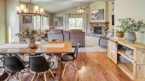 A spacious living room with a wooden dining table, black chairs, a fireplace, and a large window. - Hot Tub, Air Hockey, Foosball, Deck Lounge Near Sunriver & Mt. Bachelor Skiing (Bend)