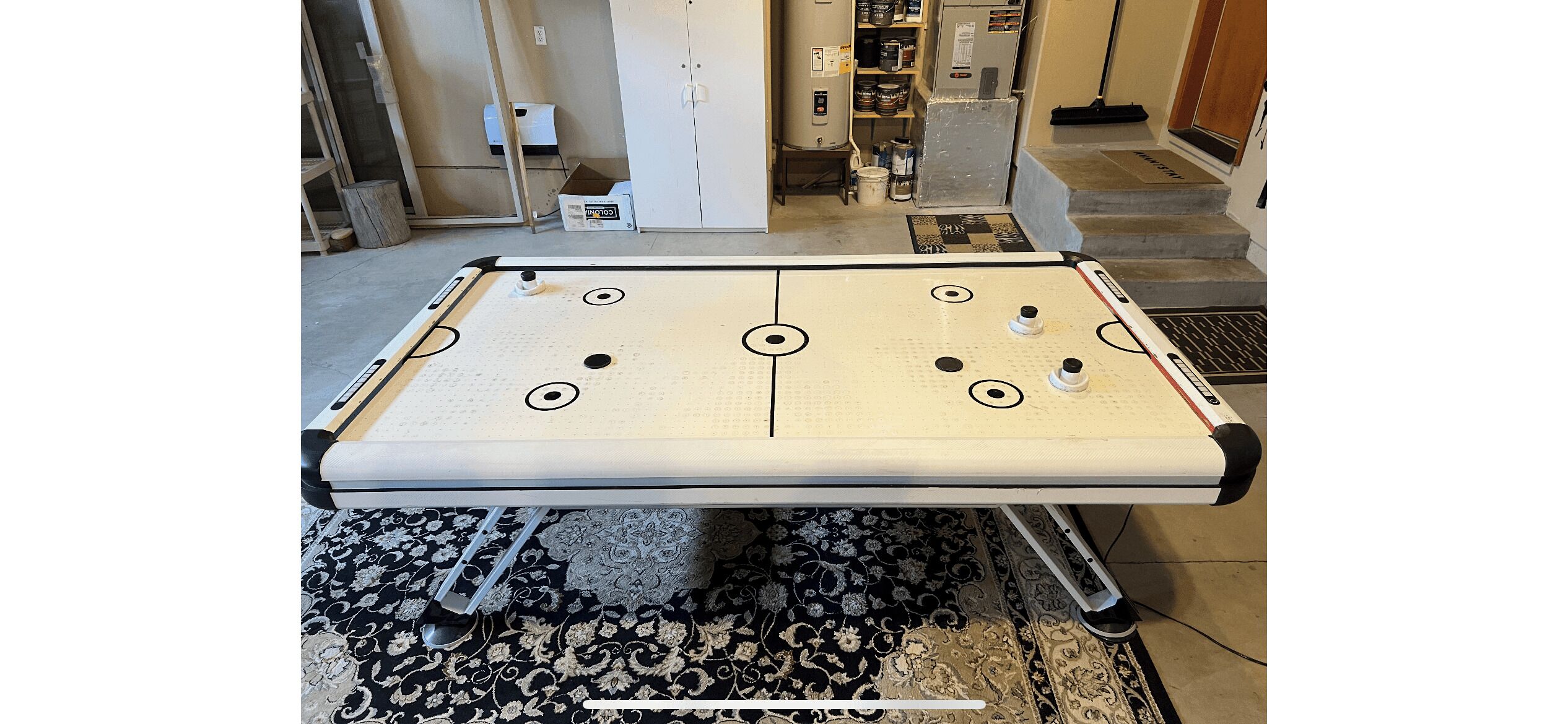 A pool table in a room with a patterned rug, a white cabinet, and a staircase.