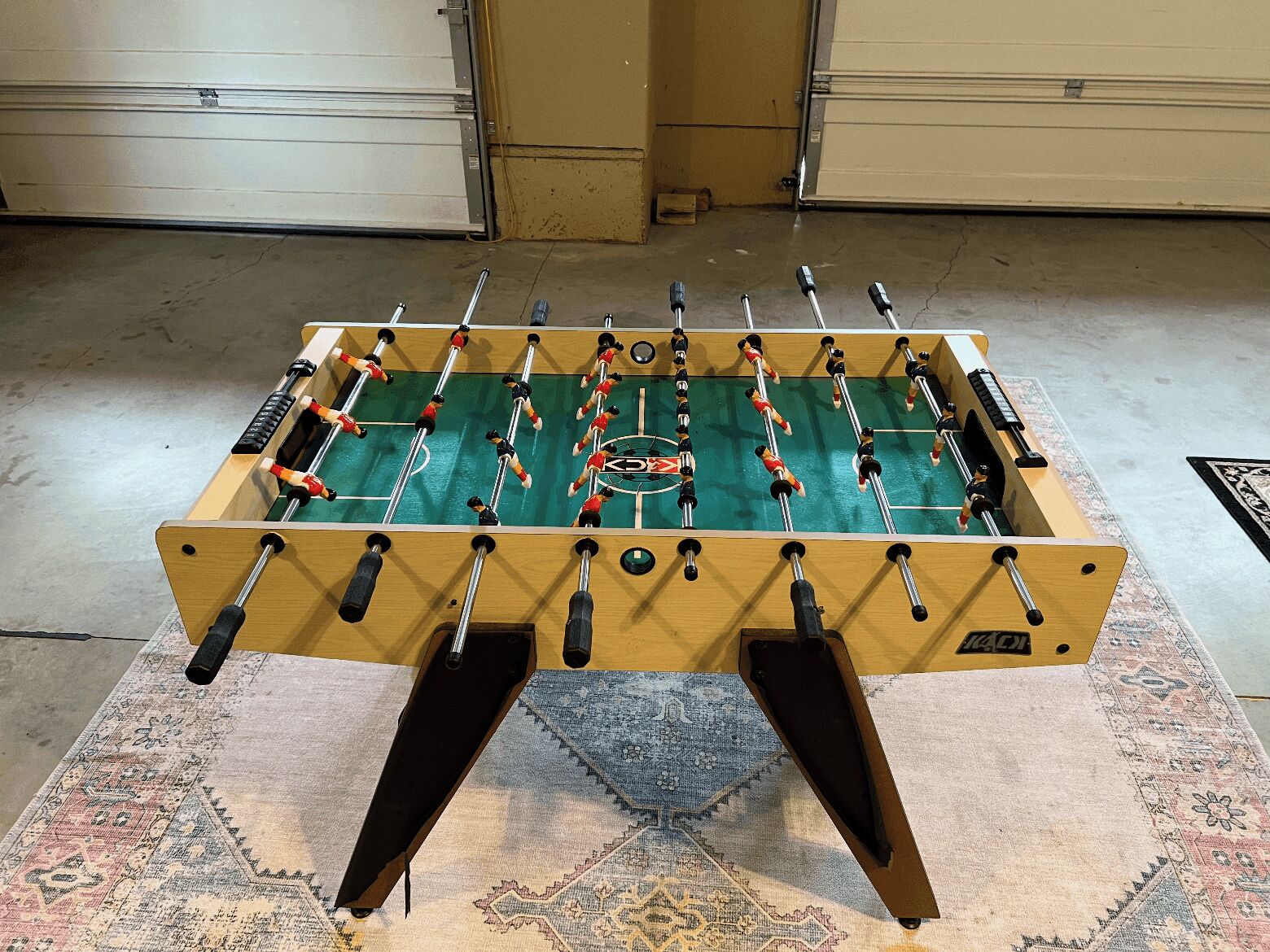 A foosball table in a room with a patterned rug and two closed storage units in the background.
