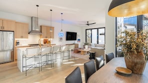 A modern kitchen with a dining area, wooden cabinets, a large island, and a view of the outside.