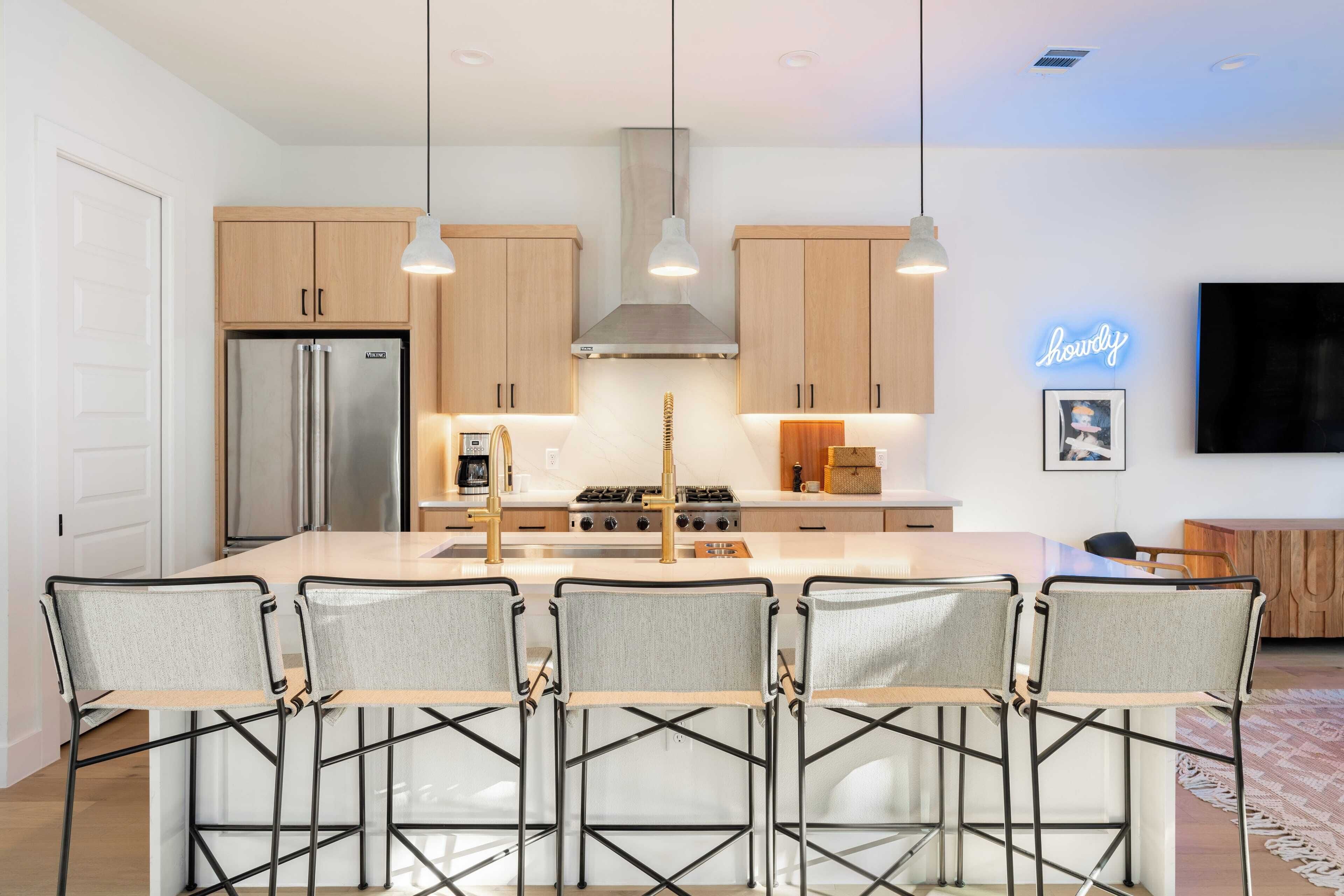 A modern kitchen with wooden cabinets, a stainless steel refrigerator, a gas stove, and a neon sign.