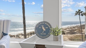 Blick aus einem Fenster auf den Strand, mit einem Schild, auf dem "BB's Blue Heron" steht, und einem kleinen Blumentopf auf einem weißen Tisch.