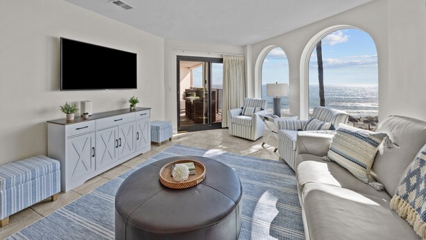 Ein modernes Wohnzimmer mit Flachbildfernseher, einer Couch, einem Couchtisch und Meerblick durch große Fenster.