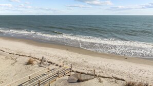 Ein Strand mit einer Holzpromenade, die zum Wasser führt, einem sandigen Ufer und einem klaren Himmel.