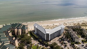 A coastal hotel with a beach view, parking, and a large building with a unique roof design.