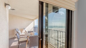 A balcony with a table and chairs, a view of the beach, and a sliding glass door.