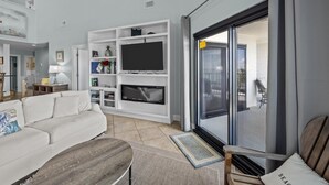 Una sala de estar moderna con un sofá blanco, un televisor de pantalla plana y un ventanal corredero que da a un espacio exterior.