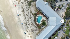 Vista aérea de un resort con una piscina grande, acceso a la playa y un estacionamiento.