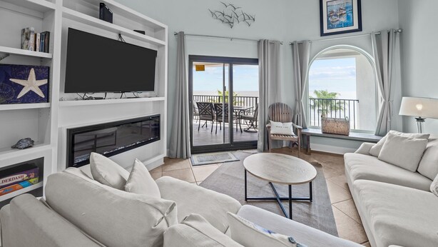 Una sala moderna con televisor de pantalla plana, asientos cómodos, un balcón con vistas y una estantería.
