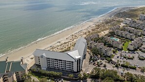 Un hotel frente al mar con vistas a la playa, varios estacionamientos y un edificio grande con techo plano.