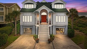 A two-story house with a prominent front entrance, a covered porch, and a driveway leading to the entrance. - Luxury Oceanfront- Private Pool, Hot Tub, & Elevator! Can't beat location! (Isle Of Palms)